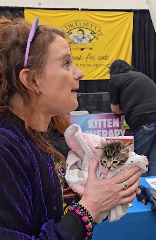 KJ holding a kitten in the Dr. Elsey's Kitten Therapy area, with the Dr. Elsey's banner behind her