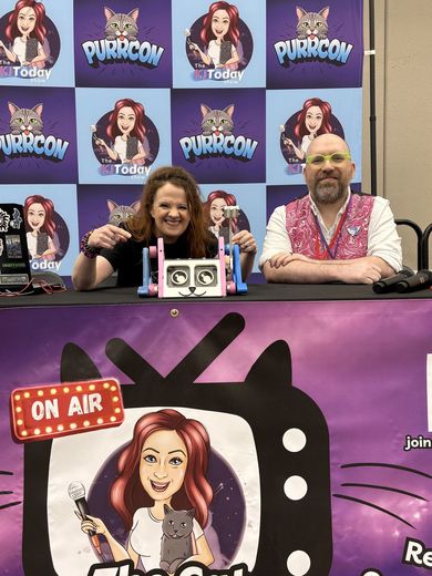 Two hosts smiling behind the On Air desk at The Cat Conversation stage