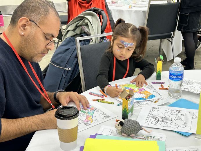 A girl and an adult coloring cat pages at a PurrCon craft table
