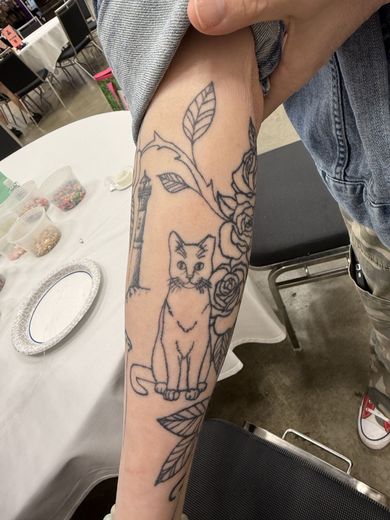 Attendee showing a cat tattoo on their forearm