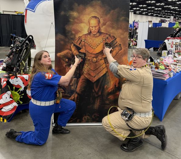 Ghostbusters cosplayers posing with a painting at PopCon