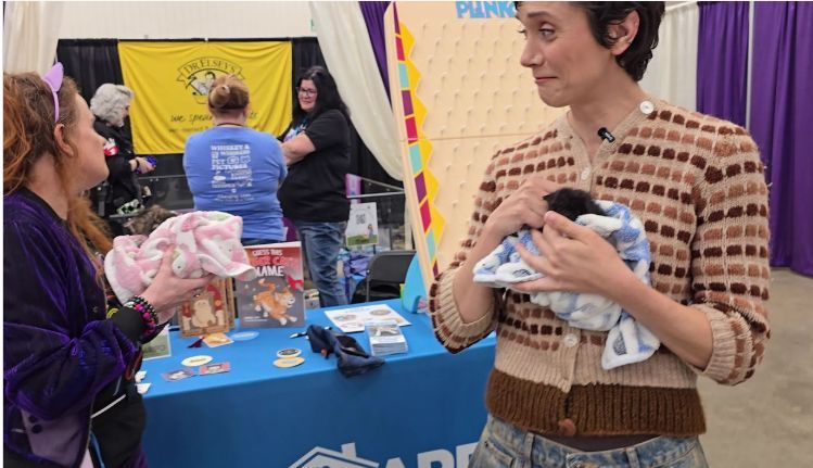 Attendee holding a kitten wrapped in a blanket at a rescue booth